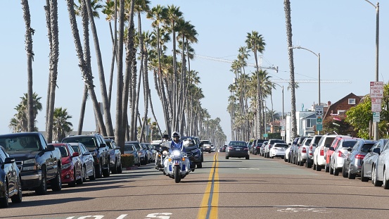 Oceanside, California USA - 16 Feb 2020: Cars and biker men on motorbikes, waterfront road. Pacific ocean tropical beach tourist resort with palm trees. Beachfront street on sunny summer day.