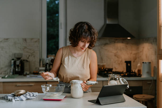 istock Home Hobbies: a Woman Baking Sourdough Bread from Scratch by Following an Online Tutorial on her Tablet 1289989028