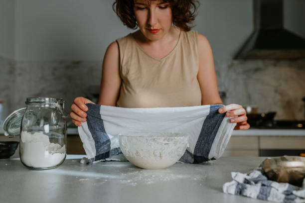 istock Home Hobbies: a Woman Baking Sourdough Bread from Scratch - Putting a Kitchen Towel Over the Dough to Let it Rest and Proof 1289989242