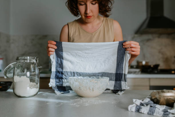 istock Home Hobbies: a Woman Baking Sourdough Bread from Scratch - Putting a Kitchen Towel Over the Dough to Let it Rest and Proof 1289989244