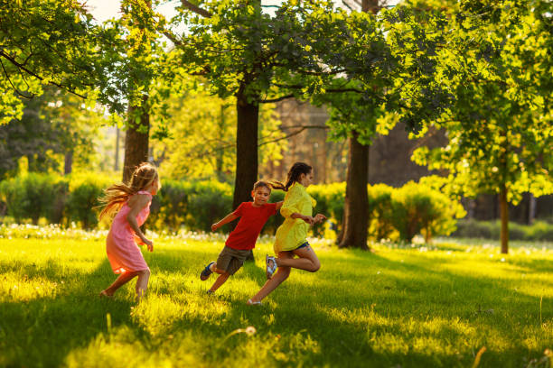 grupo de tres niños divirtiéndose jugando juego de etiqueta en el soleado parque de verano. pequeños amigos corriendo sobre hierba verde, persiguiéndose unos a otros y tratando de tocar - child running playing tag fotografías e imágenes de stock