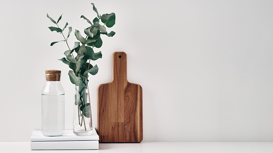 A transparent bottle with a cork stopper, a vase with eucalyptus branches and a wooden board. Natural and eco-friendly materials in interior decor. Copy space, mock up