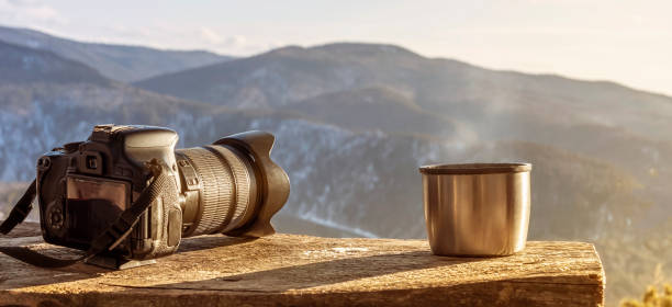 Minimalistic still life in the mountains panorama-camera and steaming mug thermos with hot tea or coffee on the background of beautiful mountains. Beautiful view, real nature and travel in winter or autumn, Hiking stock photo