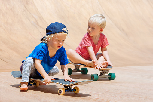 Funny skateboard riding. Little children with skateboards have fun in beach skate park. Active family lifestyle, outdoor activities on summer holidays in city. Kids recreational sports.