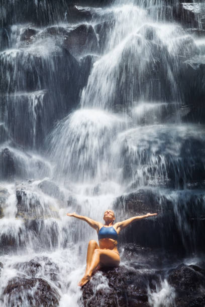 istock Woman sit on rock under cascade waterfall 1290006405