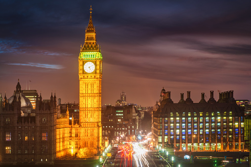 Aerial view to illuminated Big Ben and Houses of Parliament with crowded traffic on Westminster Bridge Street. Motion Blured Car and Buses Tail Lights. Twilight Sunset Night over downtown London City, United Kingdom, Europe