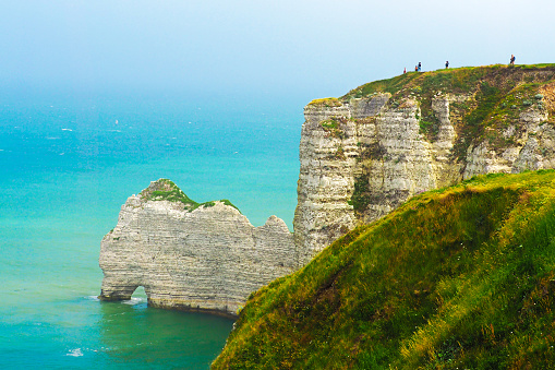Natural arch. Picturesque landscape of Etretat, Normandy, France. View from top, from the cliff down to the sea. Tops of chalk cliffs covered with green grass