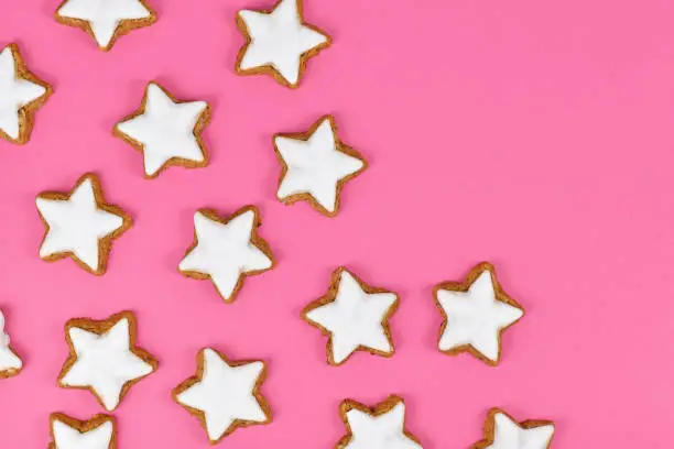 Traditional German star shaped sugar glazed cinnamon Christmas cookies called 'Zimtsterne' on pink background