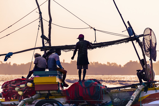 A team of fishermen on a boat prepares to fish at sunset. Sri Lanka, Weligama, 2017-12-08
