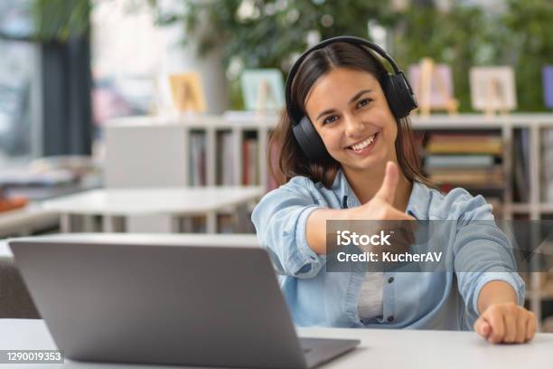 Beautiful Happy Young Woman Or Student Female Employee Sitting At Table In The University Library Or Office With Laptop Looking At Camera And Showing Thumbs Up Sign Stock Photo - Download Image Now
