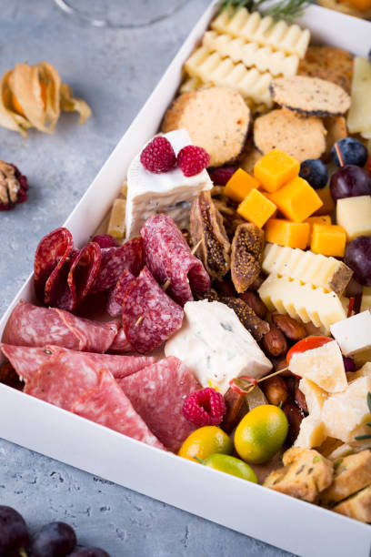 istock Cheese plate with delicious snacks. Christmas gift box with assorted cheese cubes, meat slices, fruits and nuts in gift box with crackers, olives and glass of wine 1290019620