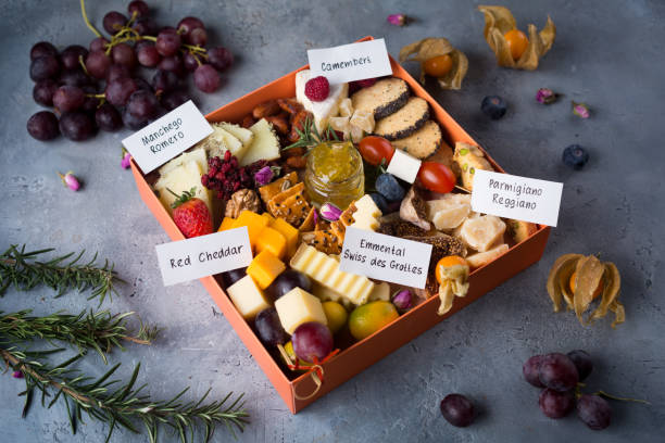 cheese plate with delicious snacks. christmas gift box with assorted cheese cubes, meat slices, fruits and nuts in gift box with crackers, olives and glass of wine - italian cuisine wine food pasta imagens e fotografias de stock