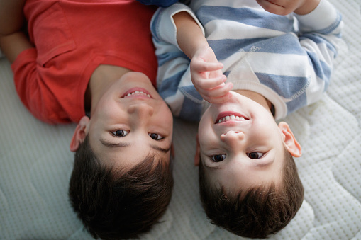 Upside down headshot of two brothers lying down on mattress without sheets and smiling
