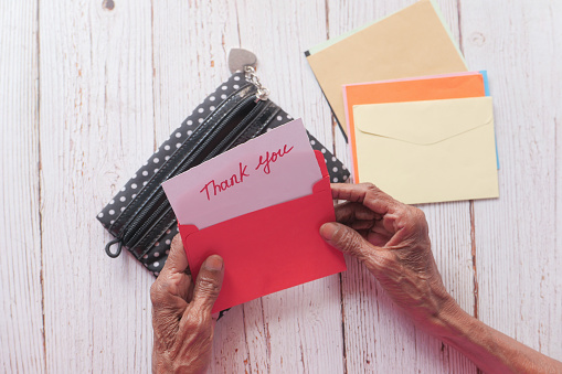 senior women's hand holding thank you note , top down .