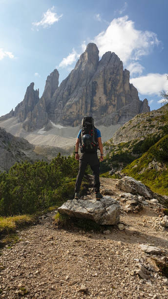 istock A man with big hiking backpack hiking in high Italian Dolomites. There are many sharp peaks behind. He is spreading his arms in the gesture of freedom. There are a few trees around. Sunny day. Outdoor 1290034442