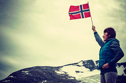 Tourist woman enjoy mountains landscape, holding norwegian flag. National tourist scenic route 55 Sognefjellet, Norway