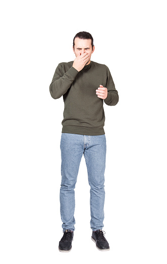 Full length portrait of a sneezing young man, covering mouth with his hand. Casual sick guy eyes closed, coughing in palm to stop spreading the viruses. Hygiene Concept.