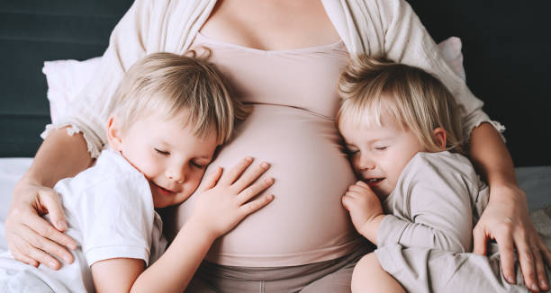 schwangere frau mit ihren kindern entspannend im bett. liebevolle mutter und kleinkinder zusammen zu hause. - third generation stock-fotos und bilder