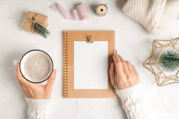 istock Desktop blank planner. Flat lay of white working table background with cup of coffee and Christmas decoration. Top view balls, fir tree, paper clips, mock up greeting card, craft Notebook and pen 1290043987