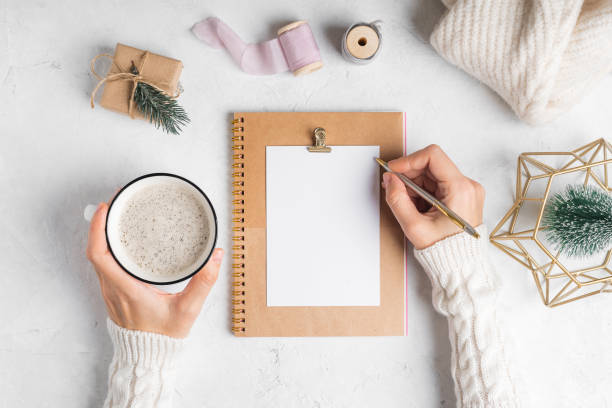istock Desktop blank planner. Flat lay of white working table background with cup of coffee and Christmas decoration. Top view balls, fir tree, paper clips, mock up greeting card, craft Notebook and pen 1290044018