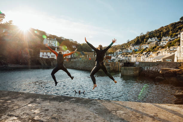 Let's Do This! A shot of a mature woman and senior man jumping into a harbour together in wetsuits at Polperro, Cornwall. staycation stock pictures, royalty-free photos & images