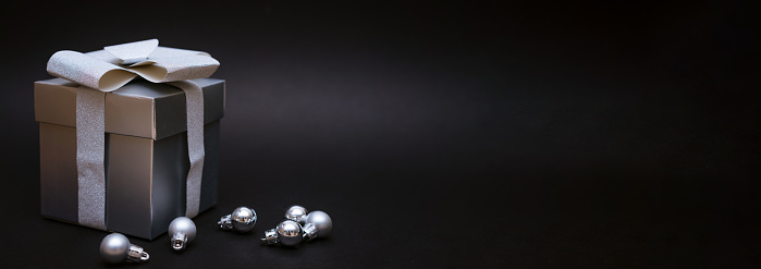 Silver gift box with christmas balls on black background, festive decor