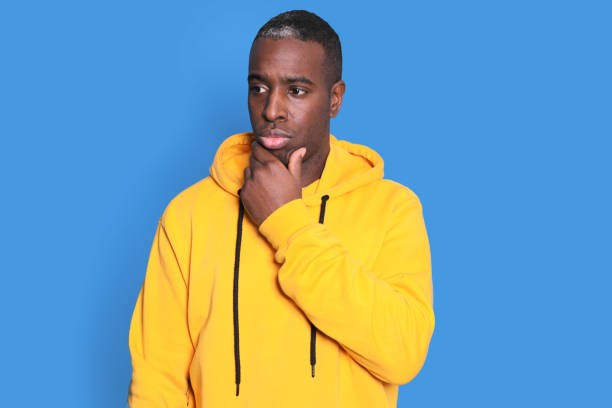 istock Pensive young man guy in casual white sweater posing isolated on blue background in studio. Mock up copy space. Put hand prop up on chin, looking away 1290049697