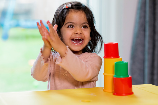 A young toddler girl playing with an early learning toy to develop her motor skills. She is in a living room and wearing casual clothing.
