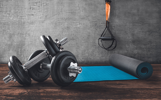 Dumbbells on wooden floor with yoga mat and TRX straps in the back.