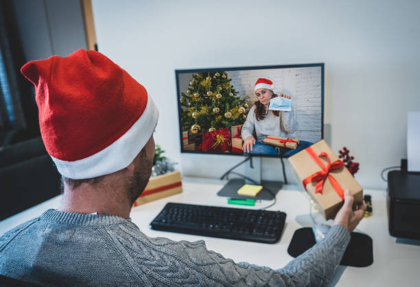 istock Sad man with mask on video call with girlfriend in self isolation missing celebrating christmas and new year face to face. Virtual celebrations and COVID-19 New Normal lockdown and social distancing. 1290055693