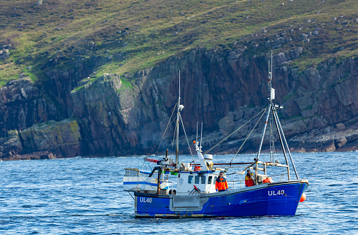 Ullapool, Scotland, August 20 2019, Fishing boat off the coast of Ullapool in the Highlands of Scotland with two fishermen on a blue boat, fishing inshore with creels.  Pre-Brexit. Horizontal.  Space for copy.