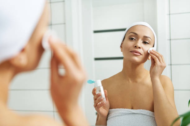 istock Woman wipes face with lotion using a cotton pad in front of a mirror 1290060676