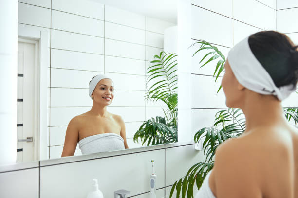 istock Young woman smiling to her reflection in the mirror while standing in her bathroom 1290060965