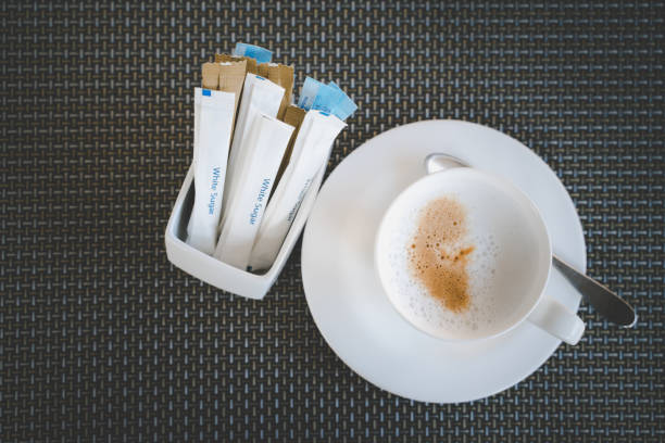 cappuccino caffè caldo e bustina di zucchero su tappetino di plastica scura, concetto dietetico, peso di perdita, vista dall'alto - sugar sachet foto e immagini stock