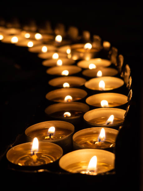 istock Tea candles in a row burning on black background 1290062603
