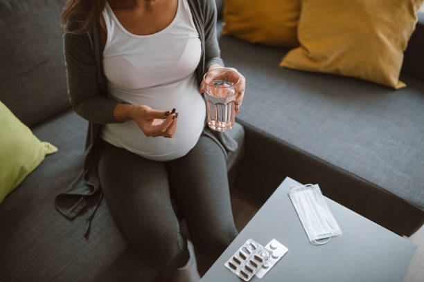 Pregnant woman drinking pills. Pregnant woman sitting on sofa at home and drinking pills. folic acid stock pictures, royalty-free photos & images