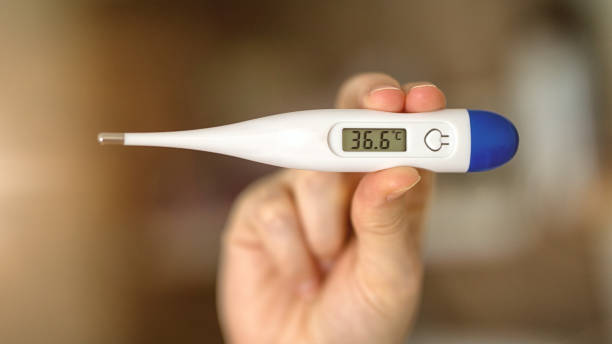 istock Woomen feeling sick holding a digital temperature thermometer with body temperature displayed. Testing and precautions virus protection concept 1290064140