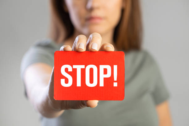 Young woman holding stop card Young woman holding red stop card on gray background"n stop single word stock pictures, royalty-free photos & images