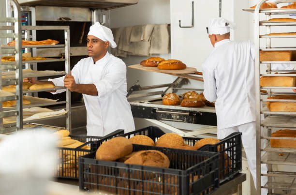 istock Man baker transporting a cart with bread in bakery 1290067802