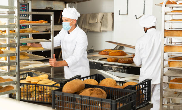 istock Man in protective mask transporting cart with bread in bakery 1290067803