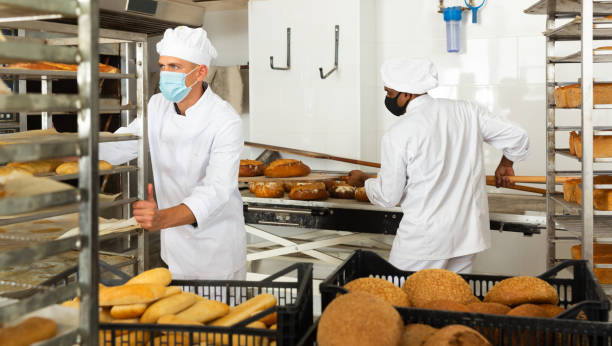 istock Man in protective mask transporting cart with bread in bakery 1290067805