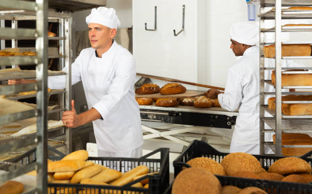 istock Male baker carrying rack trolley with bread 1290067807