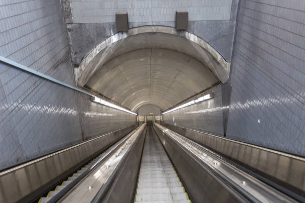 istock Silver tiled walls and escalator going deep into the ground with interesting lines 1290070190