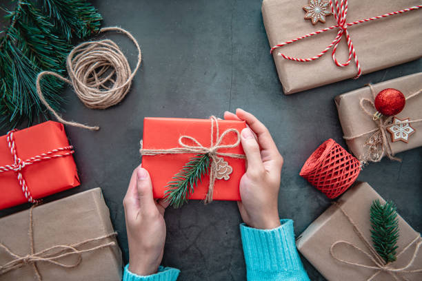 istock Hand holding Christmas gift box and tree branch decor on black background. 1290073723