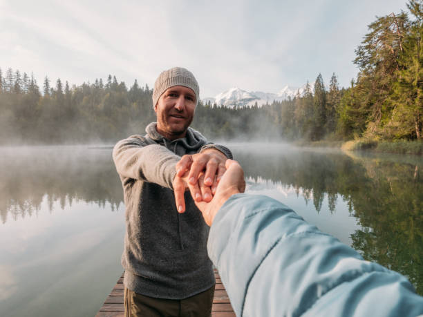 istock Man leads girlfriend onto wooden dock at sunrise 1290075193