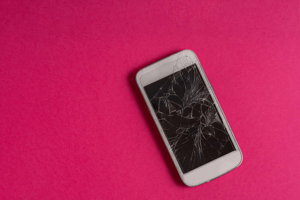 istock Broken mobile phone with cracked display on pink background, flat lay 1290080067