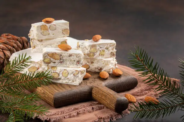 Torrone - soft italian nougat with almonds. Winter decoration. Brown background. Copy space.