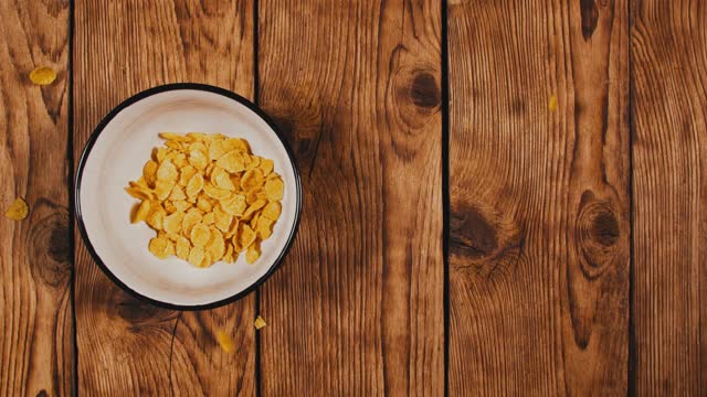 Cornflakes falling in the bowl on wooden table, slow motion. Top view