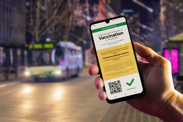 Smartphone displaying a valid COVID-19 vaccination certificate in male's hand Smartphone displaying a valid digital vaccination certificate for COVID-19 in male's hand, downtown and city bus in background. Vaccination, immunity passport, health and surveillance concepts vaccine passport photos stock pictures, royalty-free photos & images