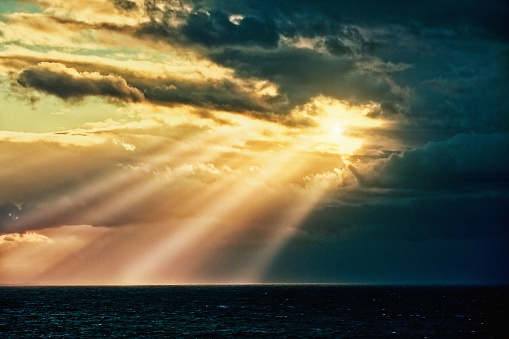 Sunbeams pour out of clouds over a beautiful calm ocean.